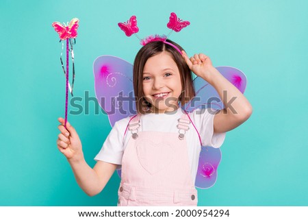 Photo of adorable cute school girl wear pink overall glasses wings smiling holding magic wand isolated teal color background