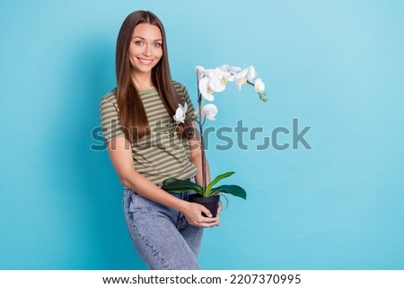 Photo of adorable gorgeous positive girl with long hairstyle wear striped t-shirt holding flower isolated on blue color background