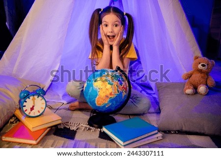 Photo of adorable impressed little preteen girl dressed casual style investigating globe sitting hovel indoors house home room