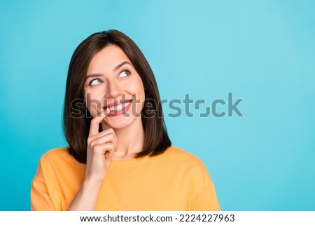 Photo of adorable minded girl finger touch lip beaming smile look interested empty space isolated on blue color background