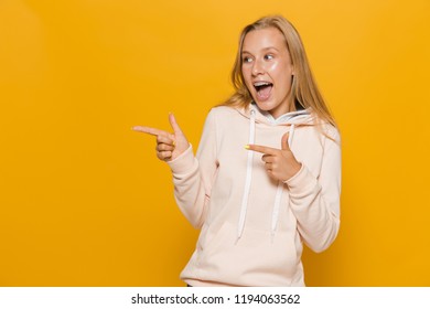 Photo Of Adorable School Girl With Dental Braces Pointing Finger Aside At Copyspace Isolated Over Yellow Background