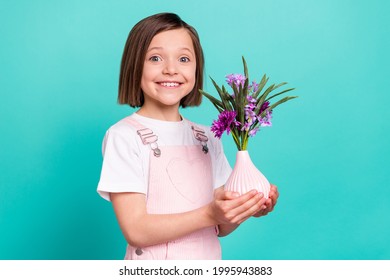 Photo of adorable shiny school girl wear pink overall smiling holding flower vase isolated teal color background