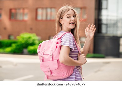 Photo of adorable sweet lady wear striped t-shirt school bag smiling waving arm hi enjoying walking outdoors urban city street - Powered by Shutterstock