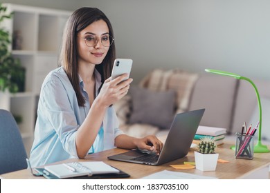 Photo of adorable young lady hold telephone look screen palm keyboard wear glasses shirt in home office indoors