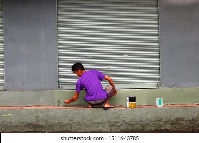 Photo of an adult Filipino man painting wall of building