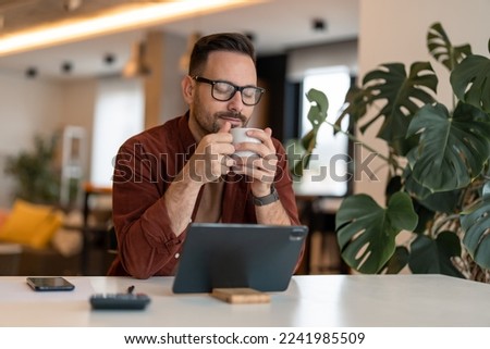 Photo of an adult man drinking coffee while having a break from work. Young content freelancer having a coffee, daydreaming with his eyes closed, smelling coffee, enjoying his break in a home office.