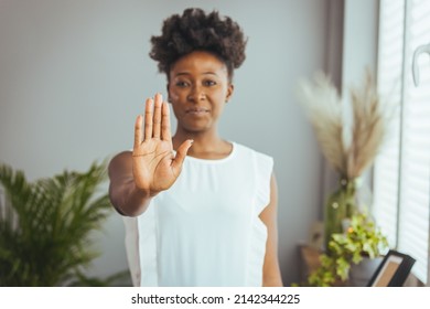 Photo of African american young woman making stop gesture with palm of her hand on grey background. Serious african american woman protesting against bullying.