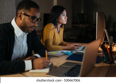 Photo Of African Businessman And Woman Working Late At Night In Their Office With Laptop And Computer.