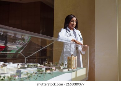 Photo of African health worker student in white coat standing next to miniature model of city under glass. Medical Student International programs worldwide