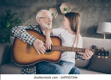 Photo of aged old grandpa little pretty granddaughter sitting comfy sofa playing guitar teaching bonding spend time together stay home quarantine safety modern interior living room indoors - Powered by Shutterstock