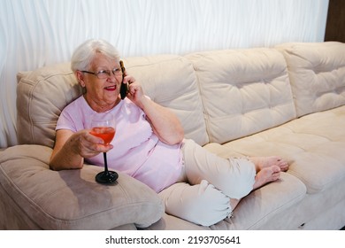 Photo of aged woman happy positive smile call talk cellphone drink alcohol wine rest relax weekend home. Senior woman at sofa talking by phone with glass of wine smiling - Powered by Shutterstock