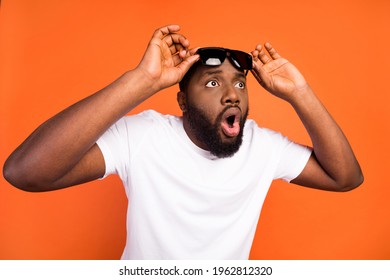 Photo of amazed astonished afro american young man look empty space hold glasses isolated on orange color background