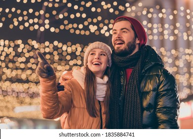 Photo of amazed girfriend point index finger evening illumination sky boyfriend, look x-mas christmas magic atmosphere wear coat scarf hat