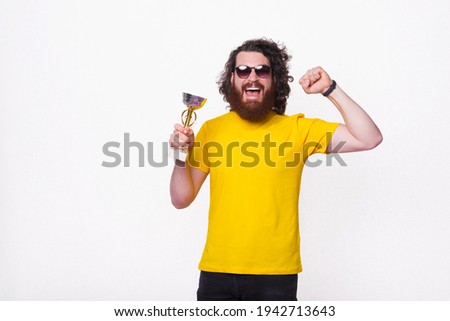 Photo of amazed and joyful bearded man screaming and celebrating and holding champion cup.