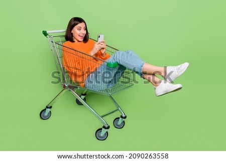 Photo of amazed lady sit pushcart search shopping website bargains wear orange sweater isolated over green color background