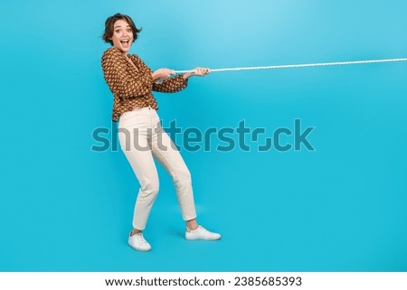 Photo of amazed positive girl pull string playing tug war game isolated blue color background
