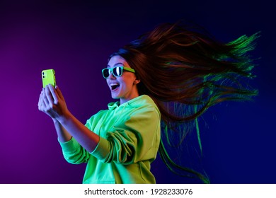 Photo of amazed shocked young woman look phone fast internet fly hair isolated on colorful neon background