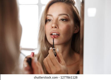 Photo Of An Amazing Beautiful Young Woman In Lingerie Underwear Looking At Mirror Apply Her Lipstick Lip Gloss Doing Makeup.