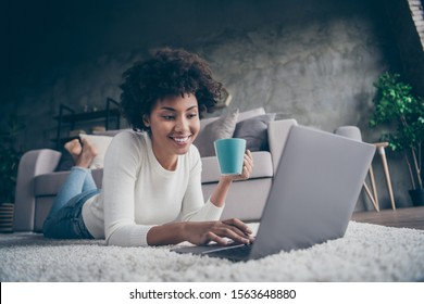 Photo of amazing dark skin curly lady  browsing using notebook texting with friends drink hot beverage lying cozy floor near sofa wear casual sweater jeans outfit flat indoors - Powered by Shutterstock