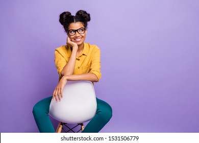 Photo of amazing dark skin lady sitting cozy on chair looking wondered side empty space wear specs yellow shirt trousers isolated purple color background