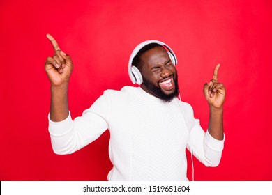 Photo of amazing dark skin man listening favorite playlist in earflaps enjoy best song moment rhythm wear white knitted sweater isolated red background