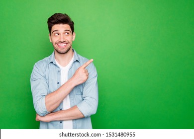 Photo of amazing salesman guy in excited mood indicating finger to empty space advising cool shopping prices wear casual denim shirt isolated green color background