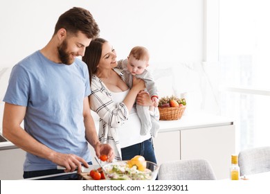 Photo of amazing young loving couple parents with their little baby son cooking in kitchen.