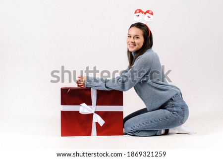 Photo of an amazing young woman in blue sweater pullover wearing christmas head hoop and sitting near big christmas gift isolated over grey background