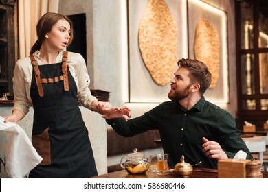 Photo Of Angry Screaming Bearded Young Man Sitting In Cafe. Looking At Waiter.