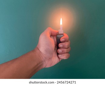 Photo of an Asian man hand holding a gas cigarette lighter with fire in a green wall background - Powered by Shutterstock