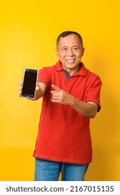 Photo Of Asian Old Man Holding An Empty Blank Screen Phone With Direct Finger Pointing To Screen Wearing Red T-shirt Isolated On Yellow Color Background