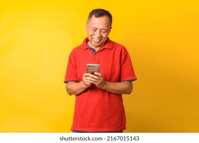 Photo Of Asian Old Man Smiling Looking On Phone Isolated On Yellow Color Background. 