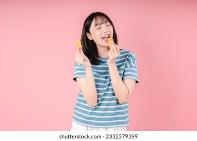 Photo of Asian woman eats appetizing fried chicken nuggets feels very hungry has fast food addiction wears stripped t shirt isolated over pink background. Unhealthy nutrition