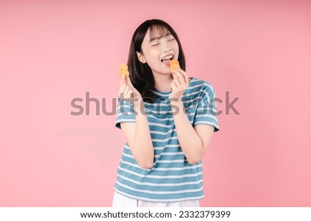 Photo of Asian woman eats appetizing fried chicken nuggets feels very hungry has fast food addiction wears stripped t shirt isolated over pink background. Unhealthy nutrition