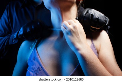 Photo of assassin killer man in black shirt and leather gloves strangling woman on black background.