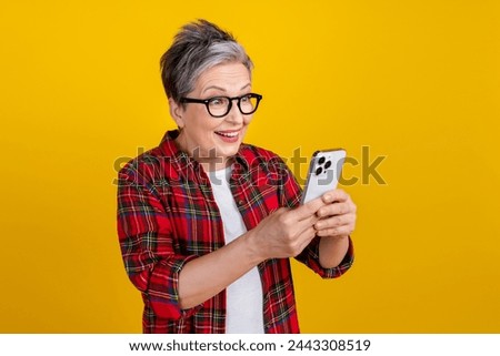 Photo of astonished cheerful lady use smart phone chatting empty space isolated on yellow color background
