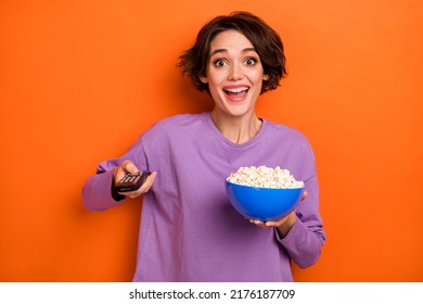 Photo Of Astonished Positive Lady Hold Popcorn Plate Remote Control Switch Channel Isolated On Orange Color Background