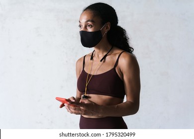 Photo of athletic african american woman in face mask using cellphone while working out indoors - Powered by Shutterstock