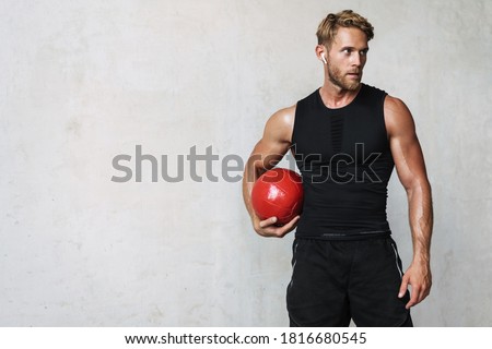 Photo of athletic young sportsman in earphones working out with medicine ball isolated over white wall