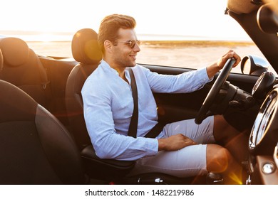 Photo Of Attractive Caucasian Man Wearing Sunglasses Driving Convertible Car By Seaside At Sunrise