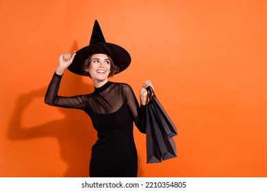Photo of attractive cheerful girl hand touch headwear hold packages look empty space isolated on orange color background