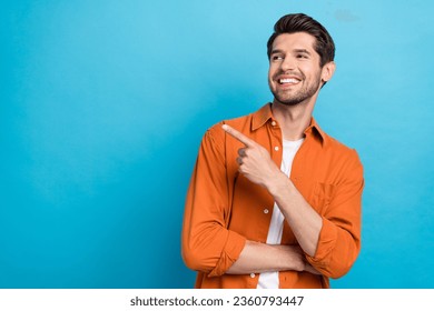 Photo of attractive dreamy man dressed orange shirt looking showing finger empty space isolated blue color background - Powered by Shutterstock