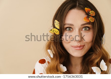 Photo of attractive excited woman with fake butterflies smiling and looking at camera isolated over beige wall