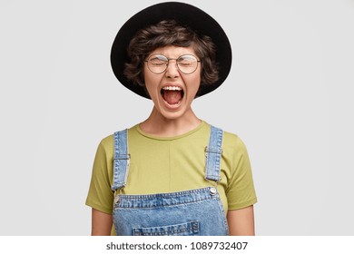 Photo of attractive fashionable Caucasian female yells loudly, keeps mouth wide opened, expresses her negative emotions, produces loud sound, isolated on white background. Annoyed angry woman screams - Shutterstock ID 1089732407