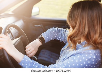 Photo Of Attractive Female Checks Time On Watch, Sits In Car, Stuck In Traffic Jam And Being Late For Meeting With Colleagues, Has To Delay It. Lovely Woman Rides Auto . People, Driving And Hurry