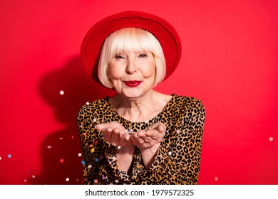 Photo Of Attractive Festive Old Lady Blow Hands Confetti Fall Wear Hat Leopard Dress Isolated On Red Color Background