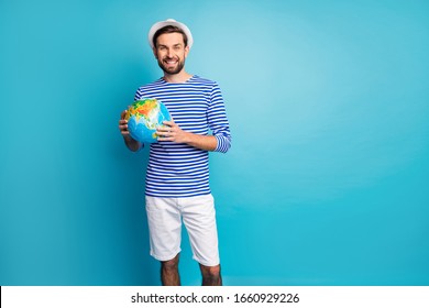 Photo of attractive funky guy holding big world globe map choosing where to travel vacation wear striped sailor shirt shorts panama pants isolated blue color background