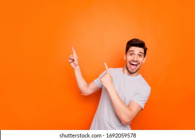 Photo Of Attractive Guy Hold Hands Fingers Direct Up Empty Space Excited Good Mood Sales Person Wear Striped T-shirt Isolated Bright Orange Color Background