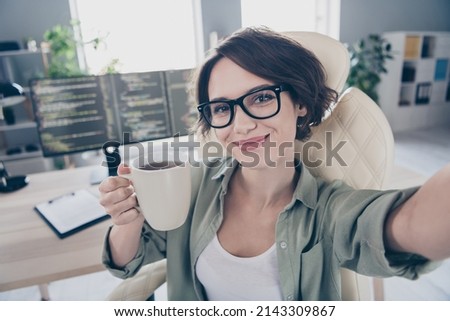 Photo of attractive happy lady sitting chair make selfie hold hot coffee cup enjoy office workplace indoors