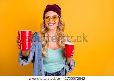 Photo of attractive lady long curly hairdo good mood students party drink beer red cup giving guest alcohol wear casual singlet denim shirt sun specs hat isolated yellow color background